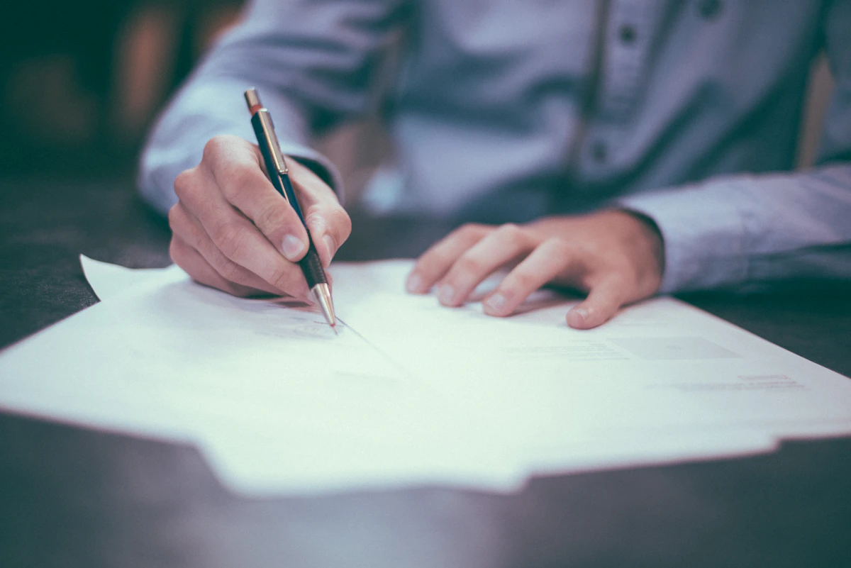 Hand writing on a paper document with a pen at a desk