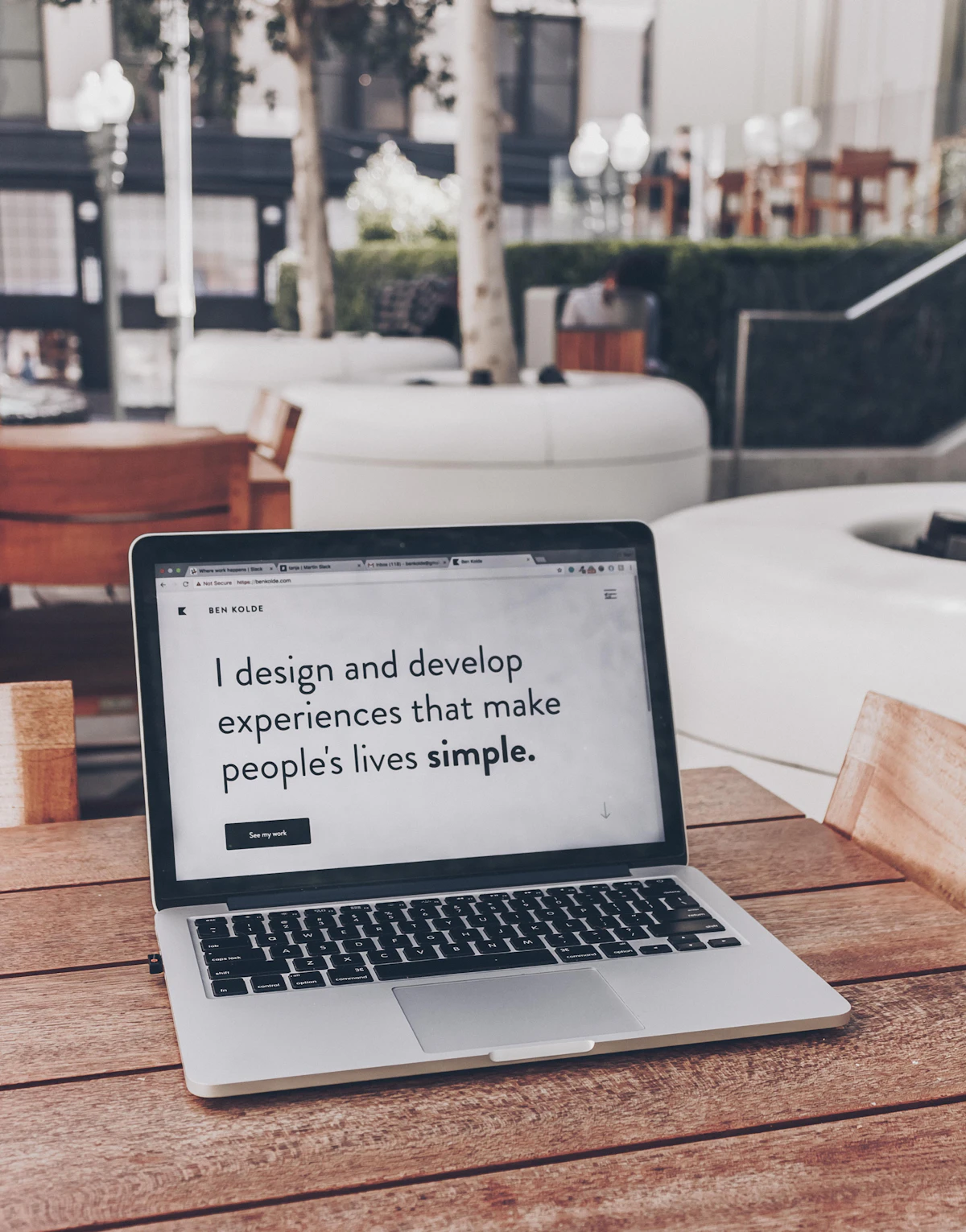 Laptop on an outdoor wooden table showing a designer's portfolio homepage