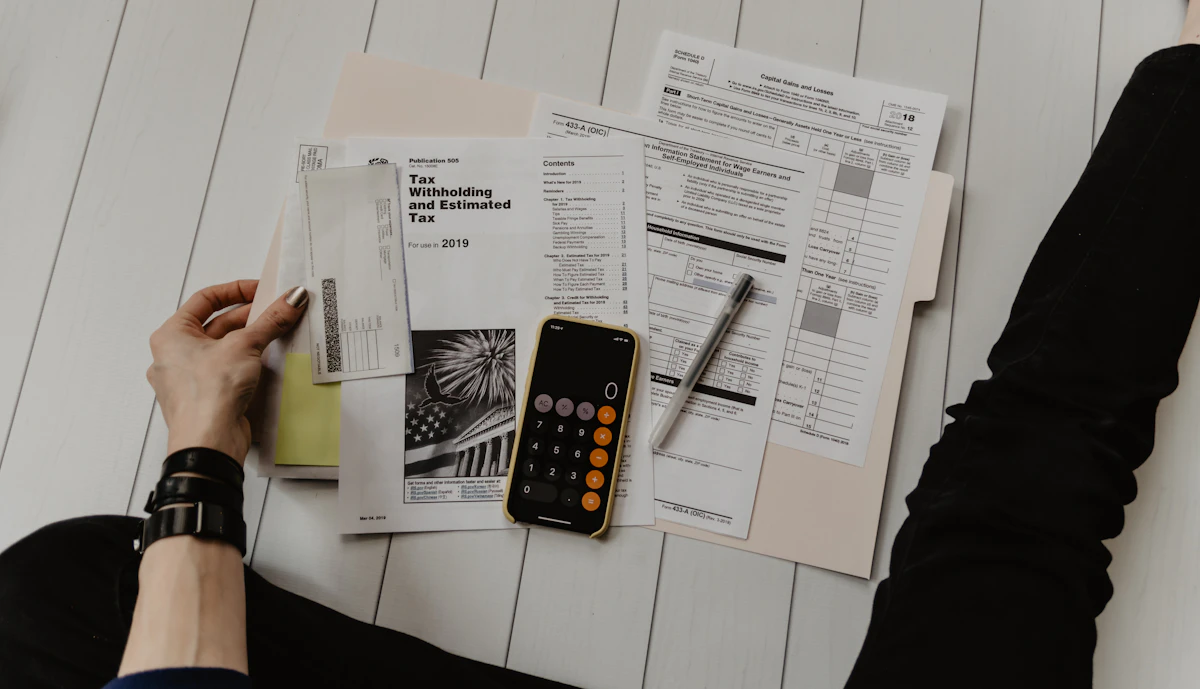 Tax forms, a phone calculator and a pen spread out on a white wooden floor