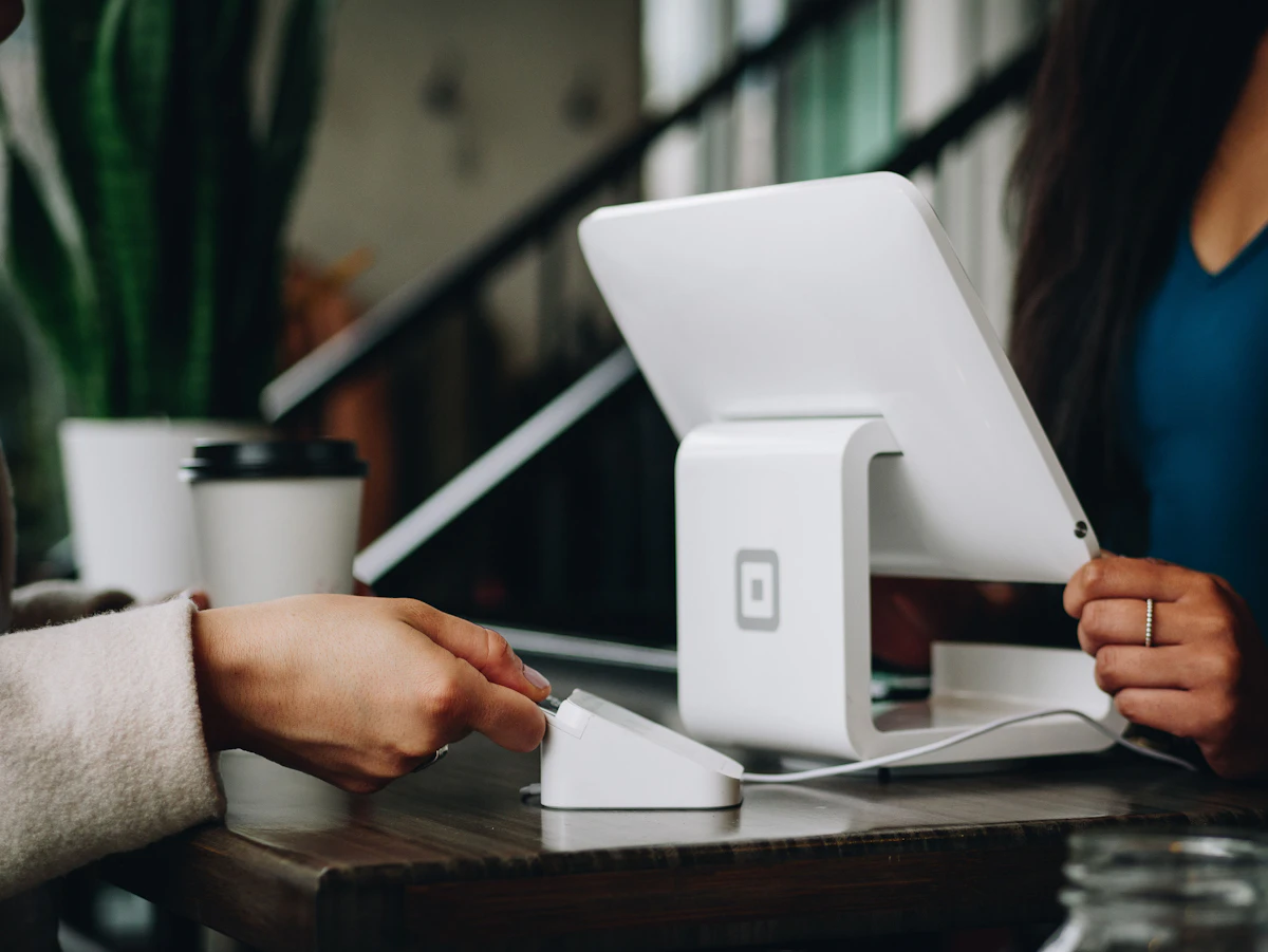 Customer inserting a card into a reader beside a white point-of-sale tablet on a wooden counter