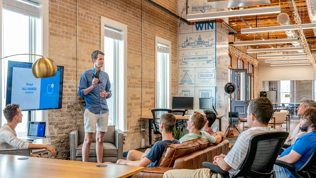 Man addressing colleagues seated on sofas at an all-hands meeting in a brick-walled office