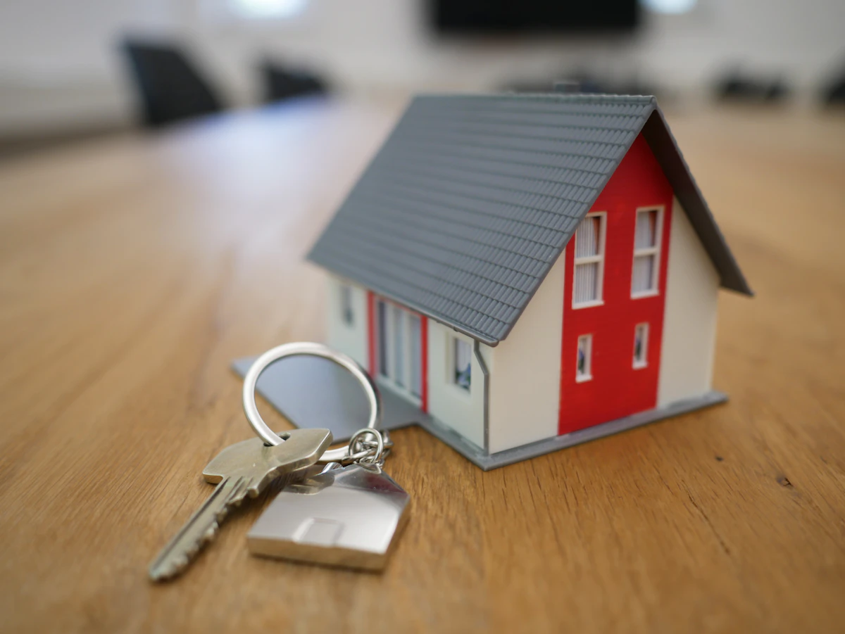 Miniature model house on a wooden table next to a key on a house-shaped keyring